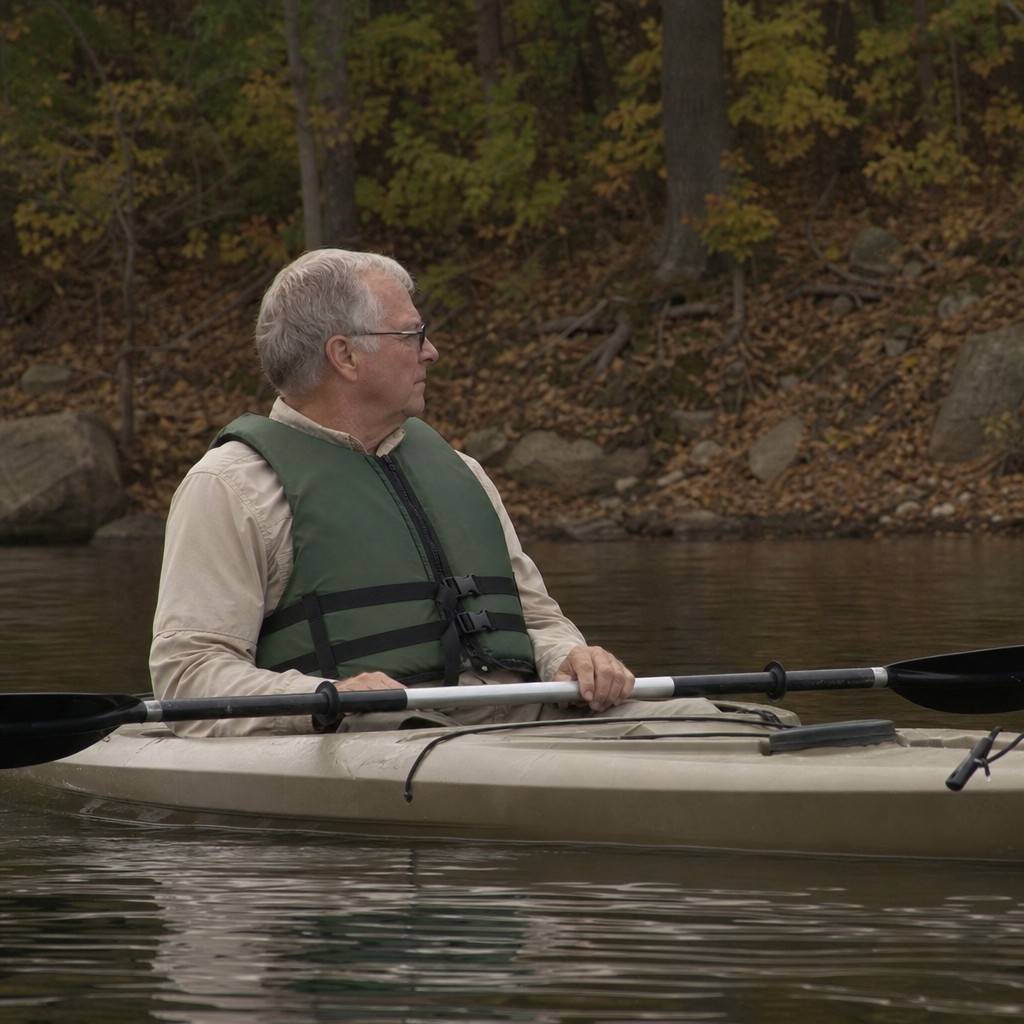 A paddler wearing a properly zipped foam life jacket in a sit-on-top kayak near shore