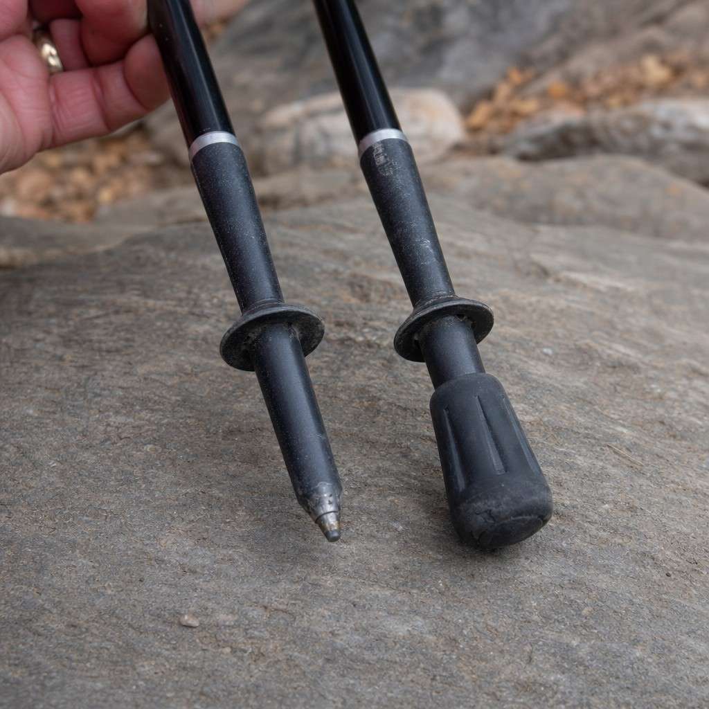 Two trekking pole tips over rock, one bare carbide point and one fitted with a rubber tip