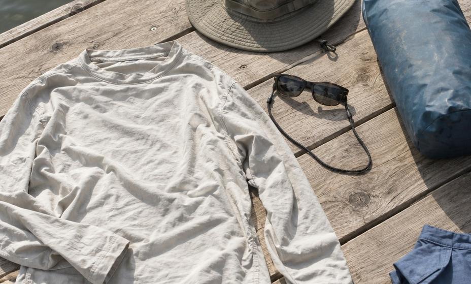 A long-sleeved shirt, brimmed hat and sunglasses laid out on a dock plank beside a dry bag