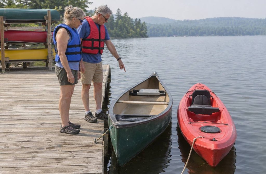 Two older adults on a lake rental dock looking at a green canoe and a red sit-on-top kayak tied side by side