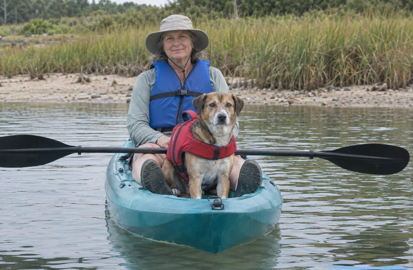 An older paddler and a medium-size dog in a life jacket sitting together in a sit-on-top kayak on calm water